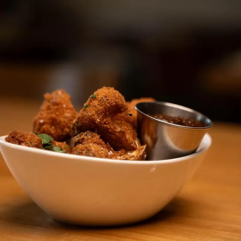 Fried golden-brown vegetable bites with dipping sauce in a white bowl.