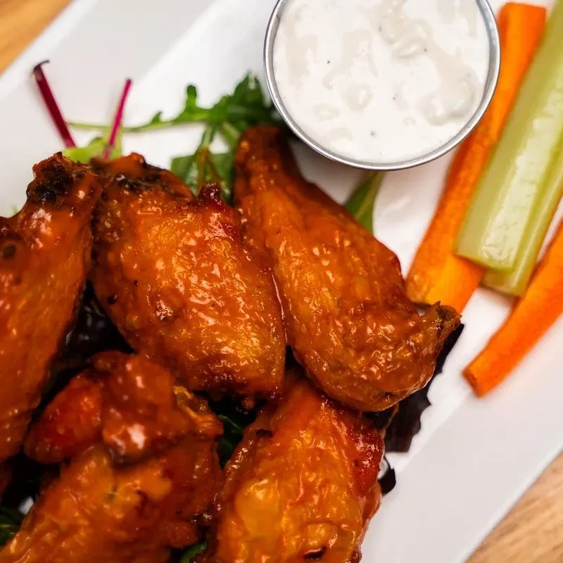 Plate of Buffalo chicken wings, creamy sauce, carrots, and celery.