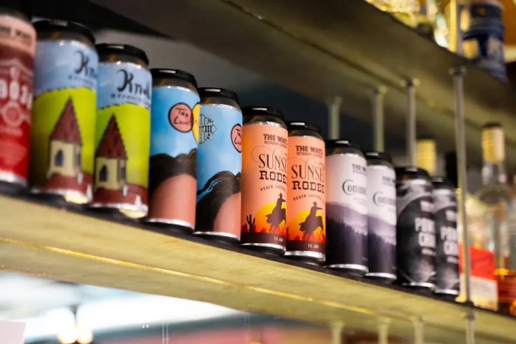 Colorful beverage cans with diverse labels displayed on a bar shelf.
