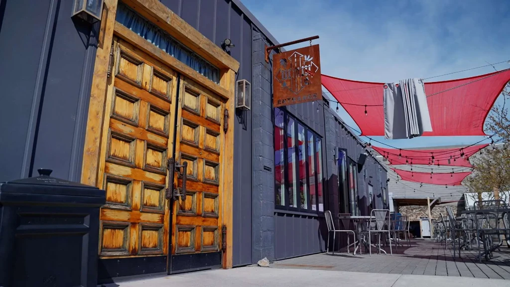 Restaurant exterior: dark metal, rustic doors, patio with red shade sails.