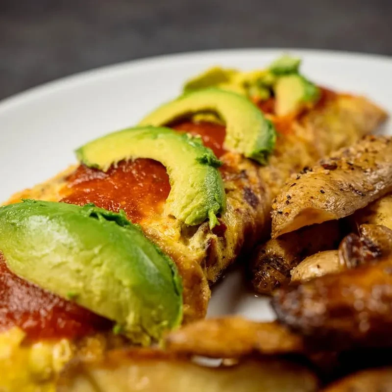 Omelet with red sauce, avocado, and a side of crispy potatoes.