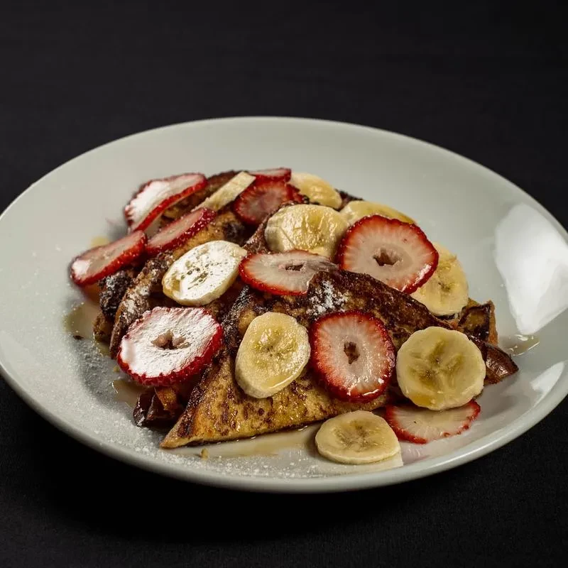 Golden French toast with red strawberries, yellow bananas, and powdered sugar.