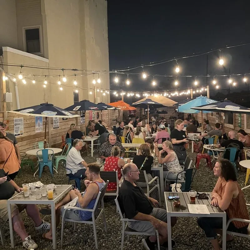 Lively night patio with string lights, colorful umbrellas, and many patrons.