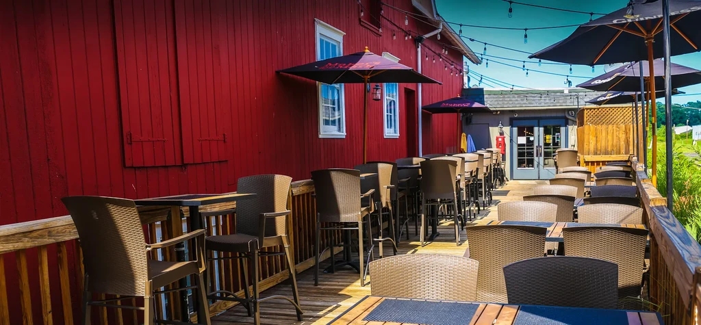 Outdoor dining patio with tables, chairs, umbrellas, and a red building.