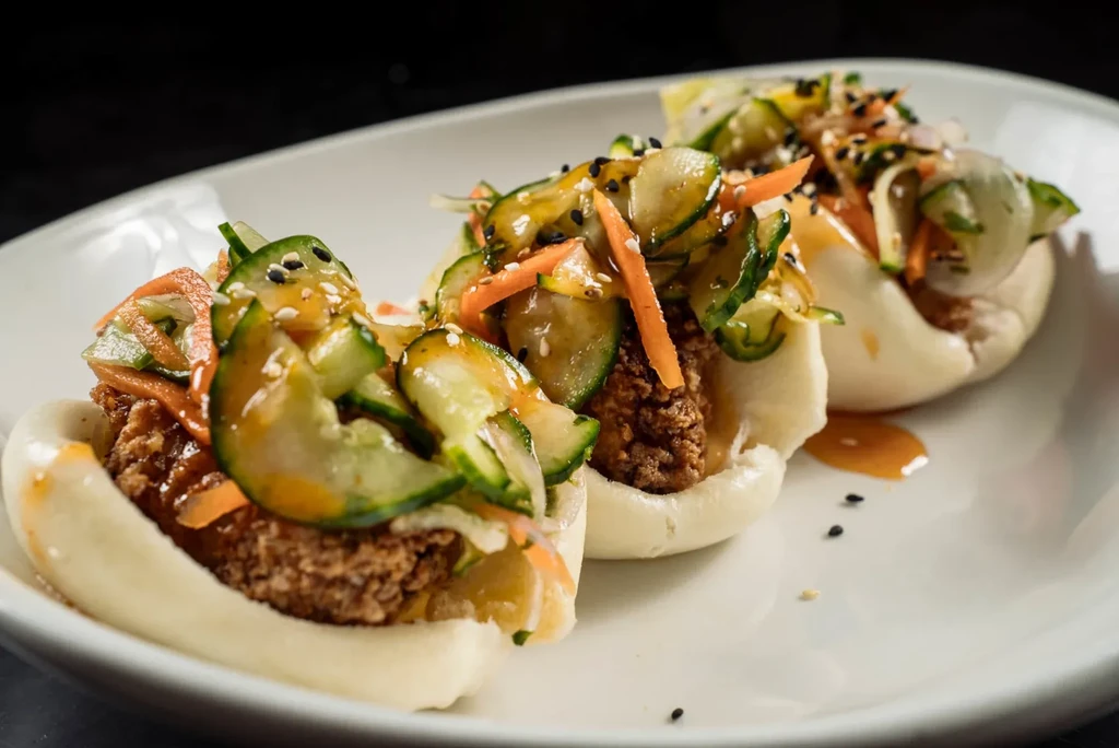 Three fried chicken bao buns with vegetables, sauce, and sesame.