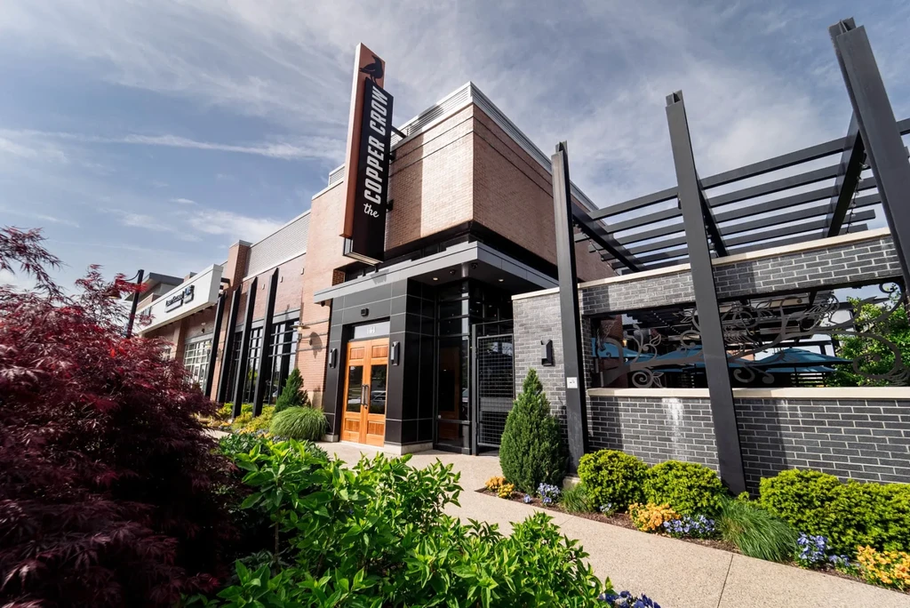 Modern Copper Crow restaurant exterior with patio and landscaping on a sunny day.