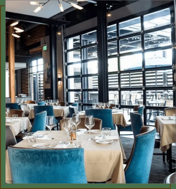 Modern industrial-chic restaurant dining room with teal chairs and large windows.