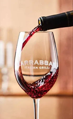 Red wine pouring into a stemmed glass etched with CARRABBA ITALIAN GRILL.