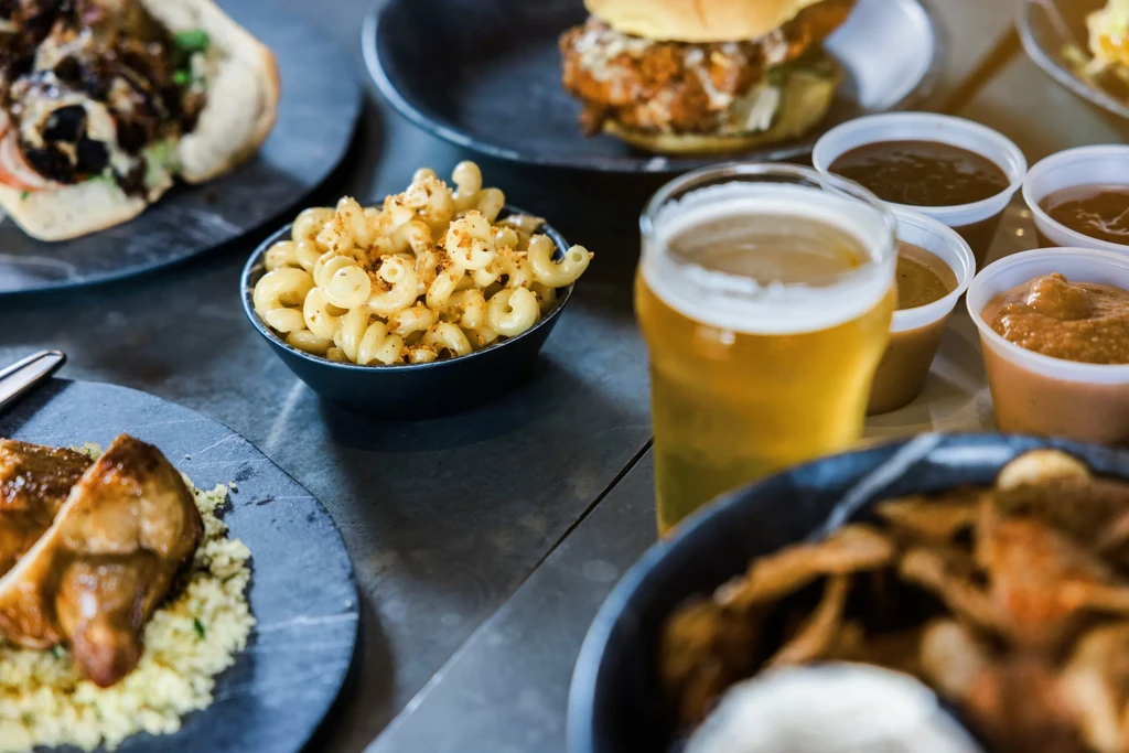 Amber beer, mac and cheese, a protein dish, and sandwich on a dark table.