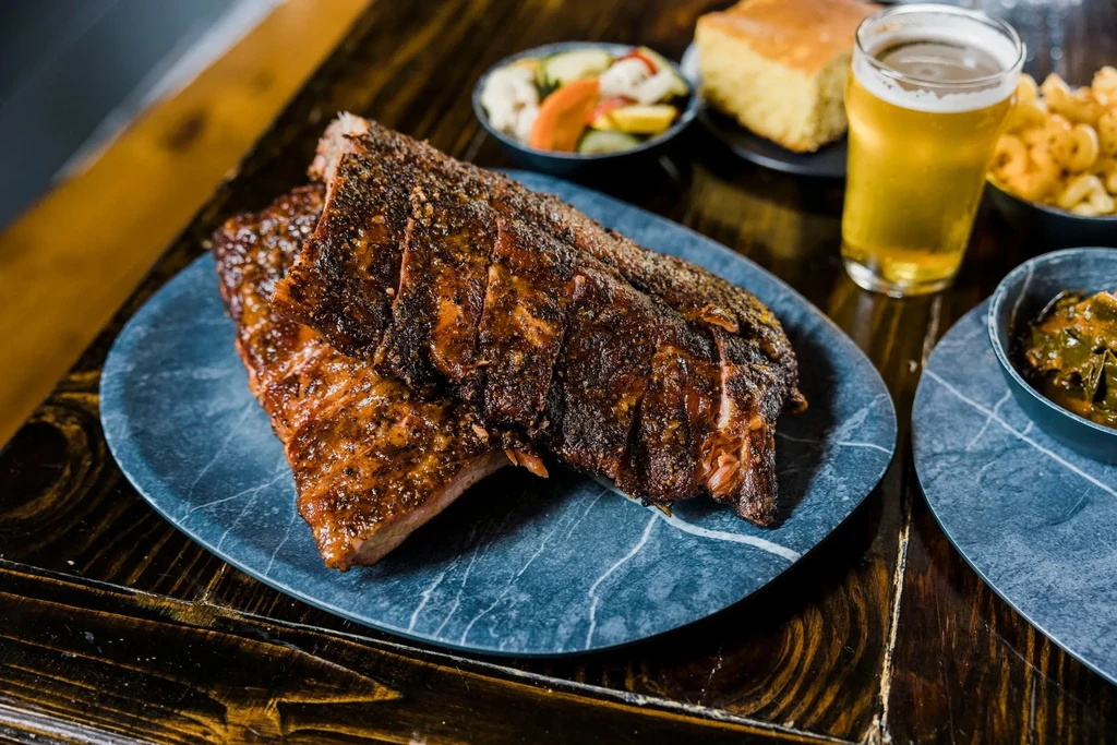 Glistening ribs, beer, and assorted sides on a wooden table.