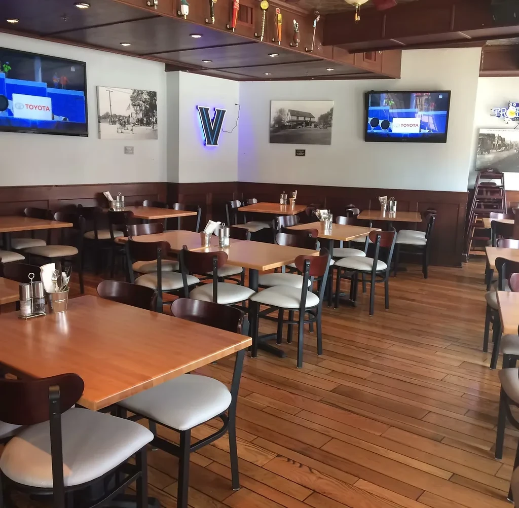 Empty casual dining restaurant with wooden tables, chairs, and sports on TVs.