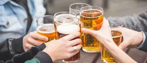Six hands toast with various beers in tall glasses.