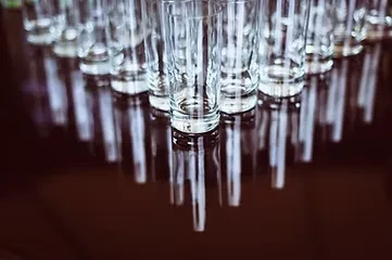 Rows of empty, clear glass tumblers on a dark reflective surface.