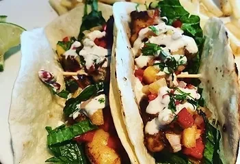 Plate of two tacos with grilled protein, fruit salsa, and lime.