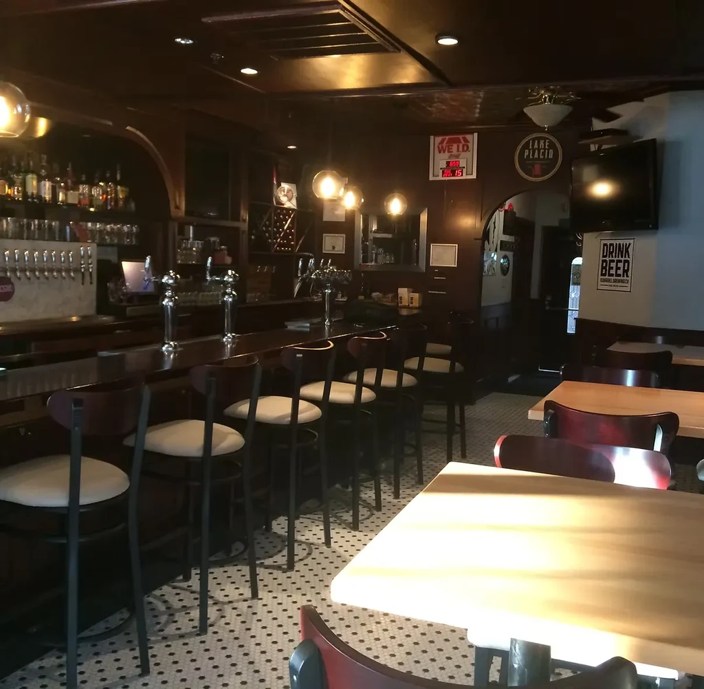 Empty pub interior with dark wood bar, beer taps, and warm lighting.