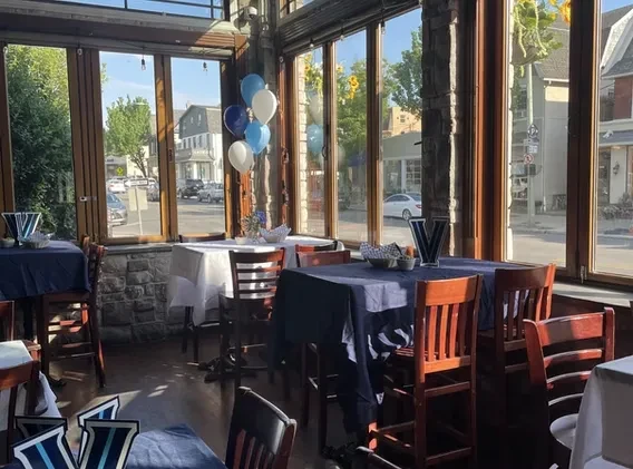 Bright, empty restaurant dining room with decorated tables and a city view.
