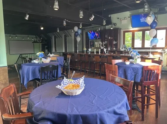 Empty casual restaurant interior, event setup with blue tables and bar.