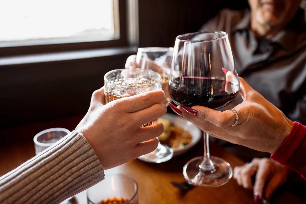 Three hands clinking glasses of amber drinks and red wine.