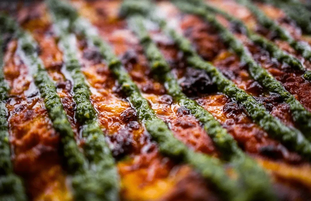 Close-up of a baked dish with reddish base and green stripes.