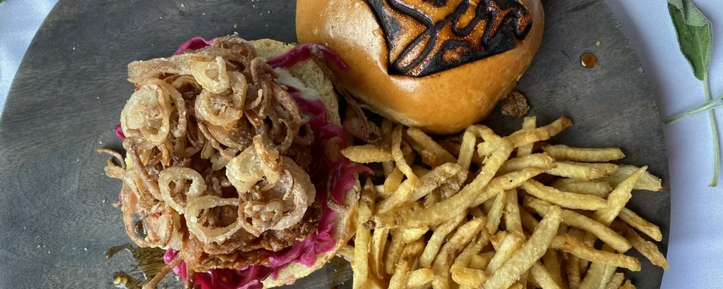 Open gourmet burger, crispy onions, red slaw, fries on a board.