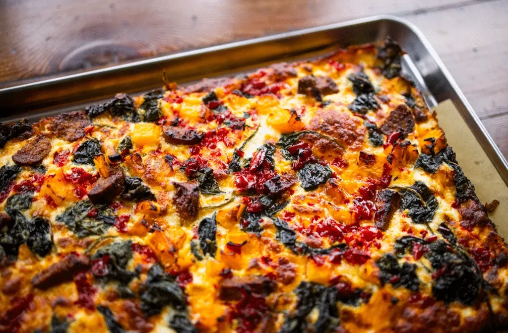 Golden rectangular baked dish with squash, greens, and meat in a pan.
