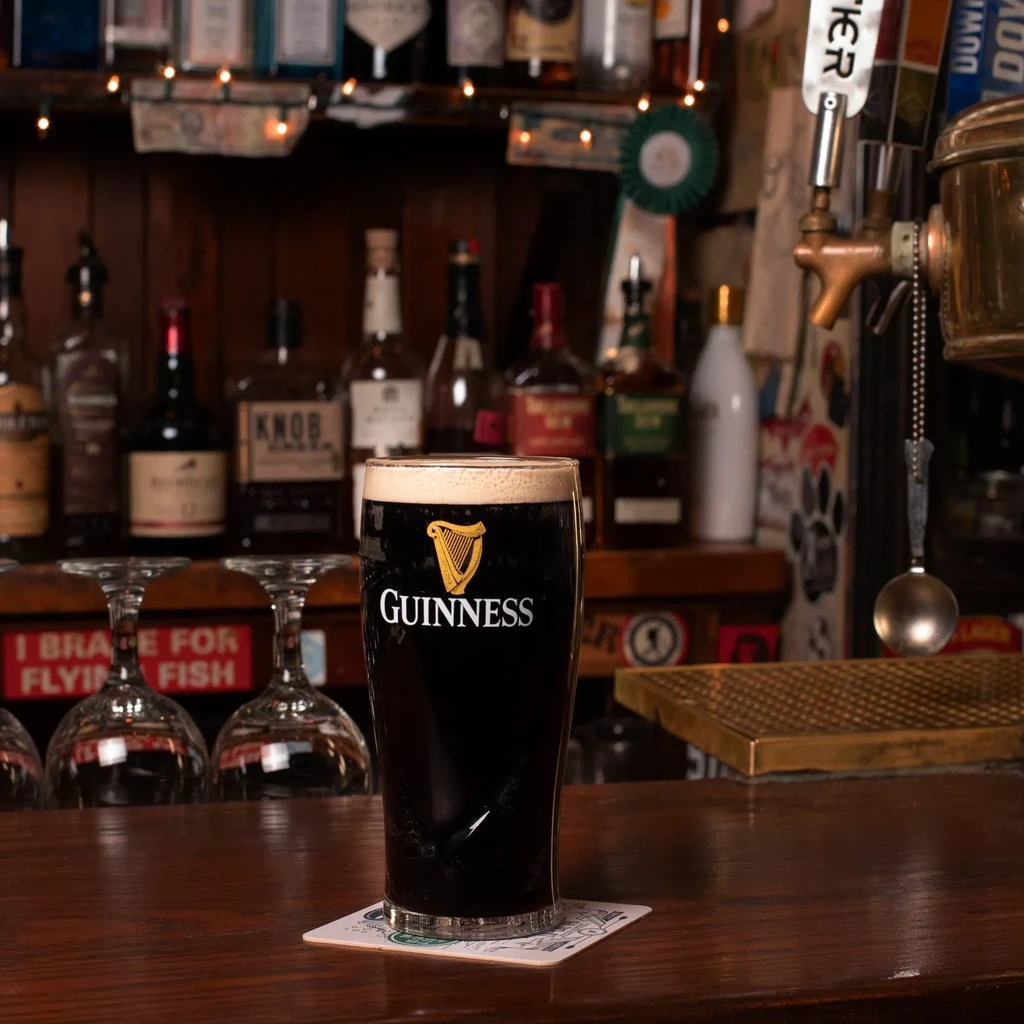 Pint of Guinness stout with a creamy head on a wooden bar.