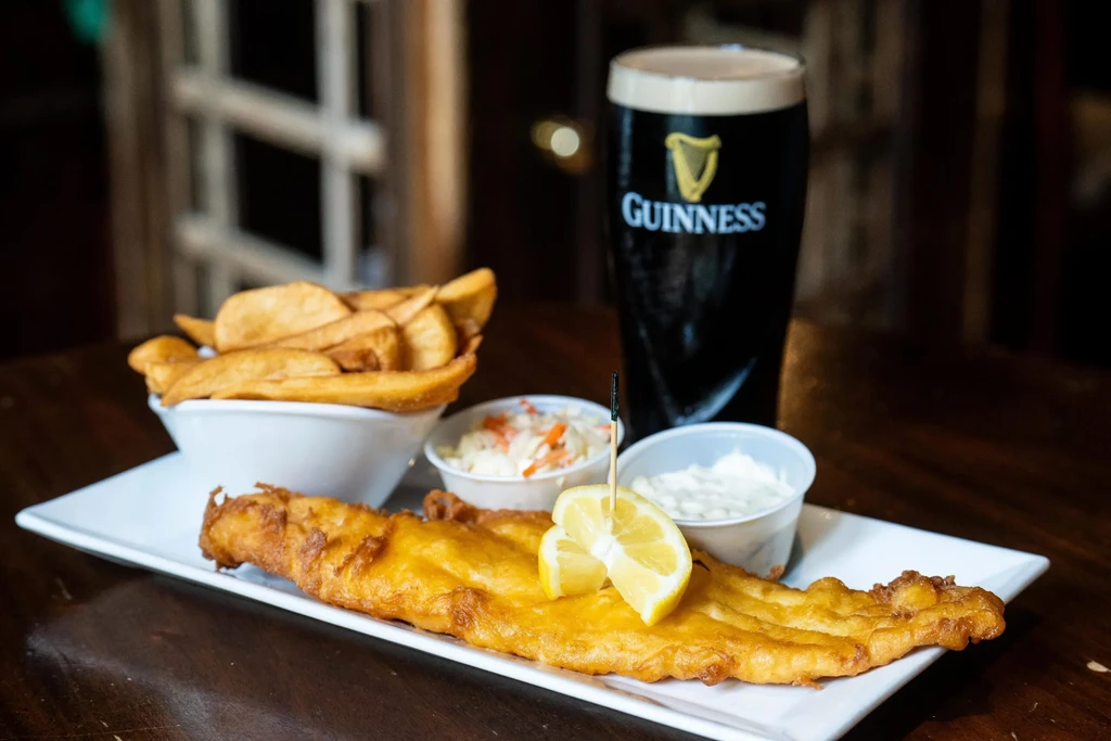 Plate of golden fish and chips, coleslaw, tartar, and Guinness beer.