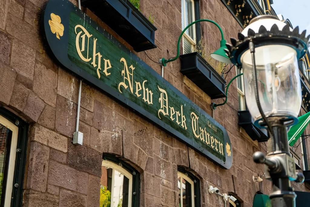 Ornate sign 'The New Deck Tavern Est. 1933' on stone building.