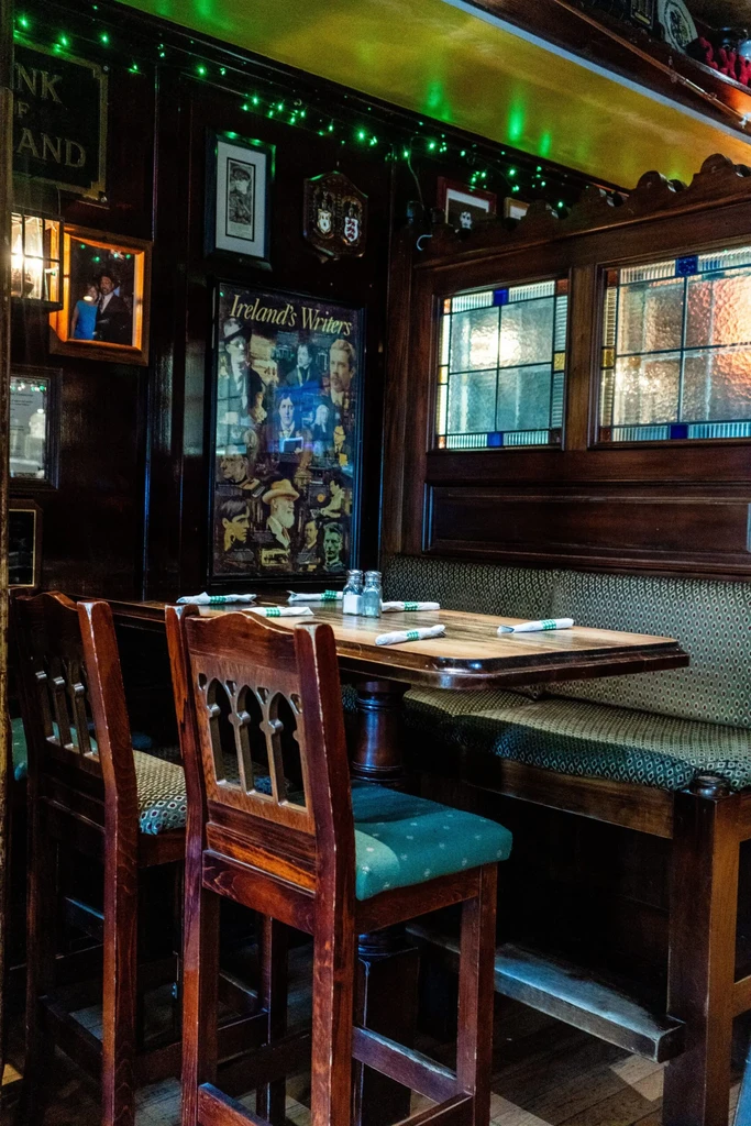 Traditional Irish pub corner with wood paneling, booth, and literary poster.