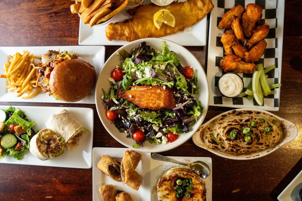 Overhead view of diverse restaurant meals on a rustic wooden table.