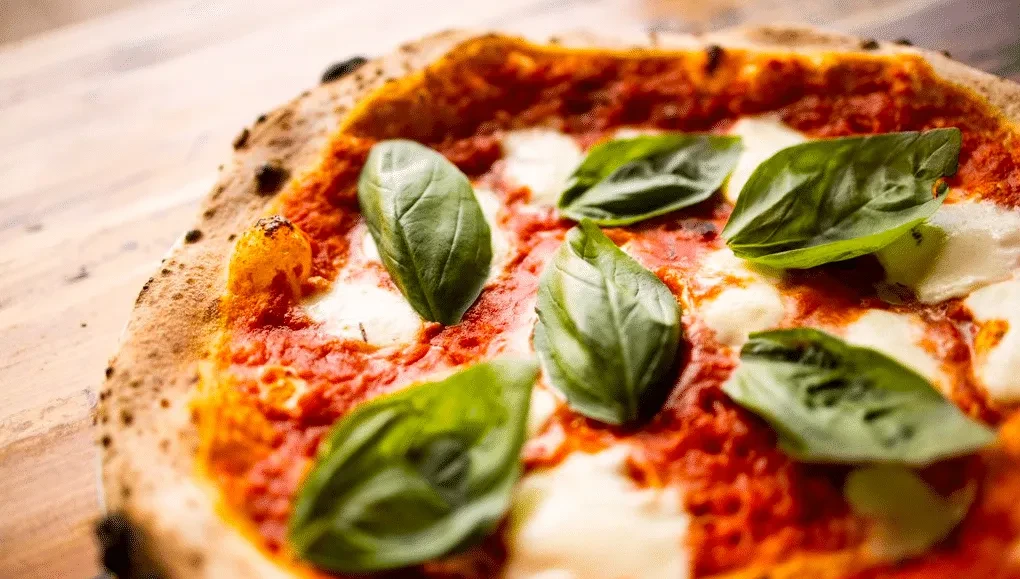 Close-up of a wood-fired Neapolitan pizza with tomato, mozzarella, and basil.