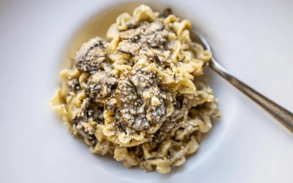 Creamy pasta with mushrooms, cheese, and herbs in a white bowl.