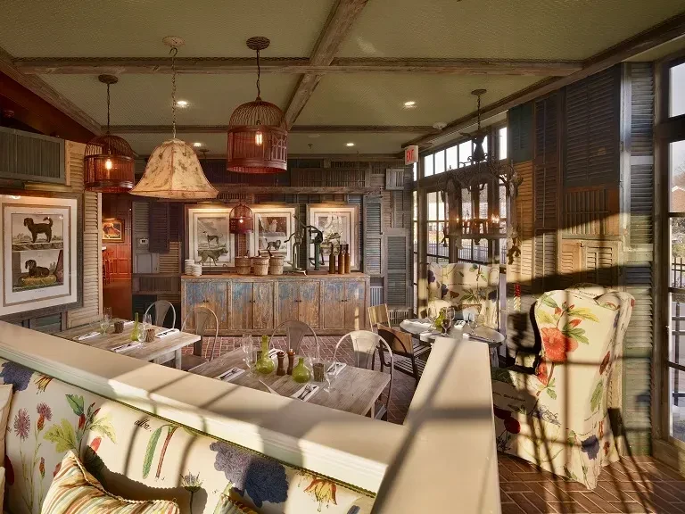 Rustic restaurant with repurposed wooden shutters, floral seating, and terracotta floor.