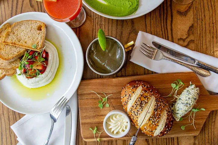 Overhead of a wooden table with gourmet spreads, breads, and drinks.