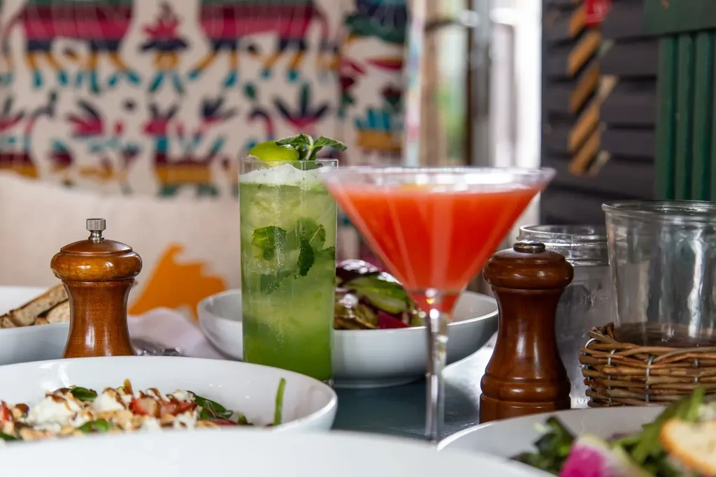 Close-up of a vibrant table with cocktails, salads, and pepper grinders.