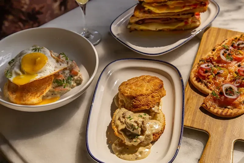 Overhead view of a diverse brunch spread with biscuits, sandwiches, and flatbread.