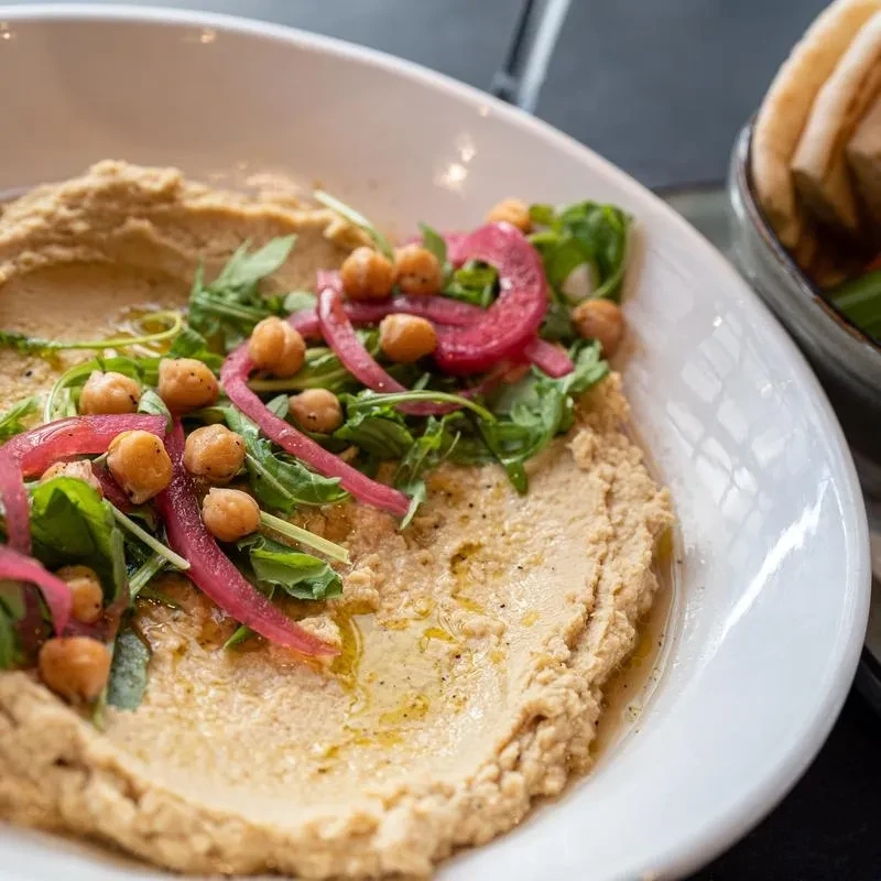 Hummus bowl with chickpeas, arugula, pickled onions, olive oil, and pita.