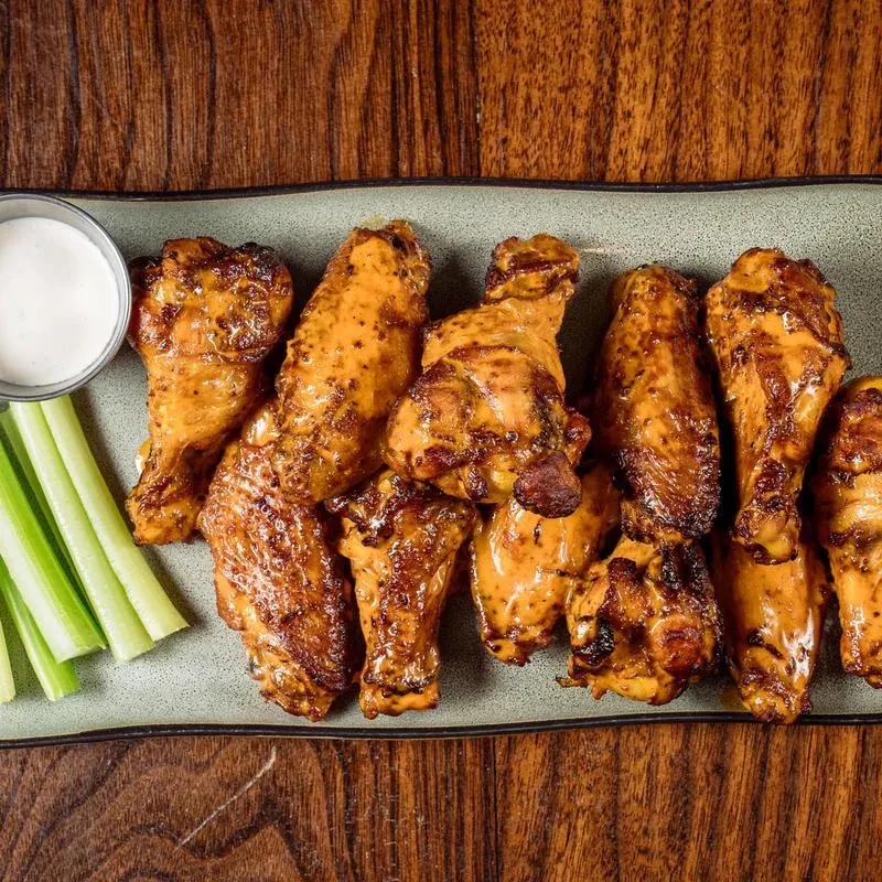 Crispy sauced chicken wings, creamy dip, and celery on a wood table.