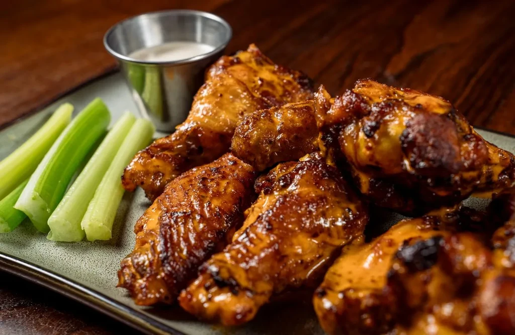 Plate of glazed chicken wings, celery sticks, and creamy white dipping sauce.
