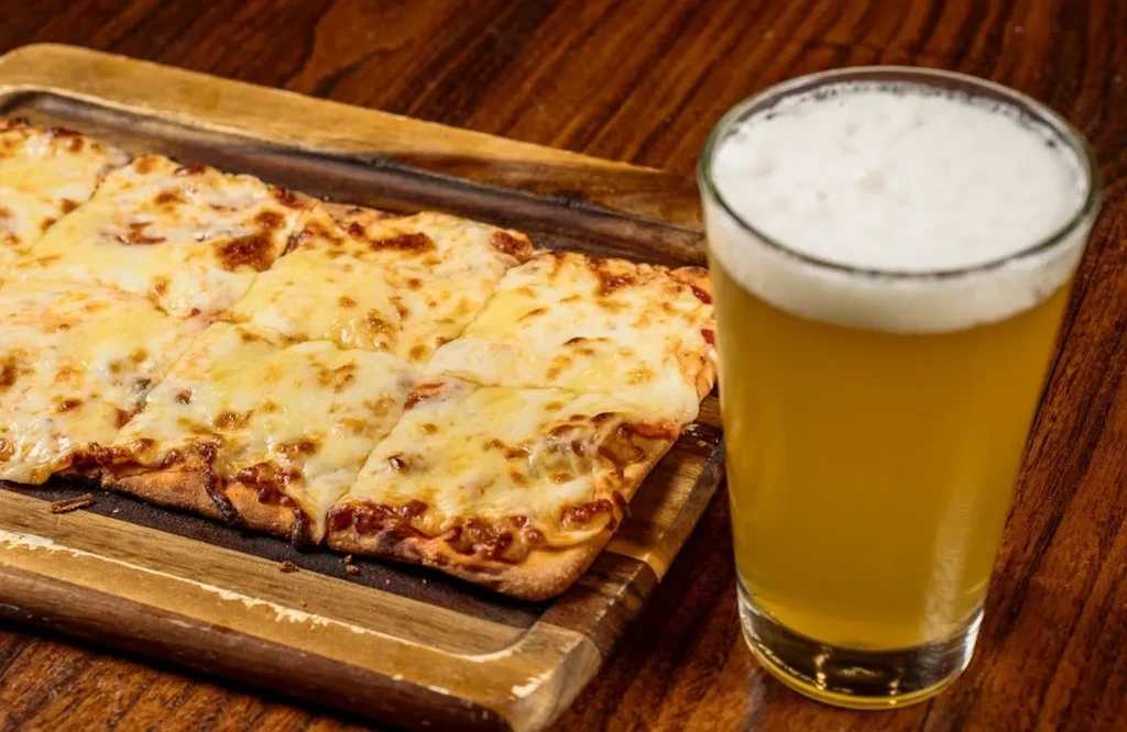 Overhead shot of cheesy flatbread slices and a foamy beer on wood.