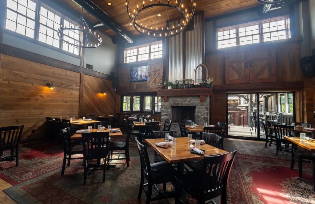 Spacious rustic lodge restaurant interior, stone fireplace, empty tables.