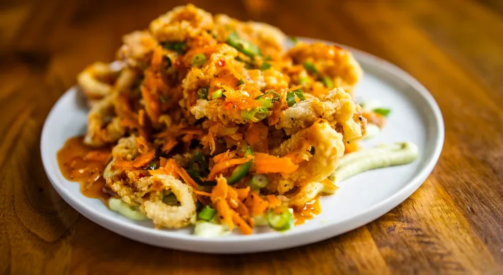 Fried calamari piled on white plate with two sauces and vegetable garnish.