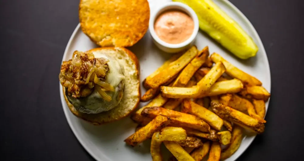 Gourmet burger, cheese, caramelized onions, fries, sauce, and pickle.