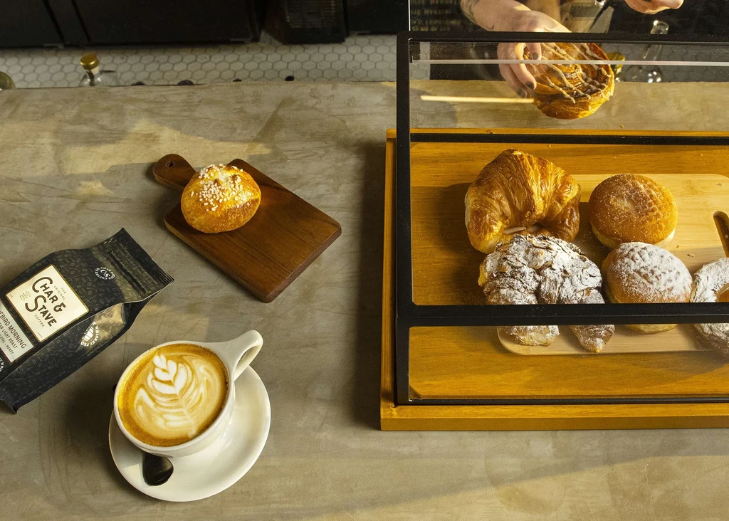 Cafe counter overhead: latte, coffee beans, pastries, hands in display.