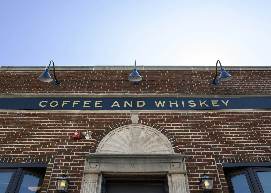 COFFEE AND WHISKEY sign on a brick facade with carved "21."