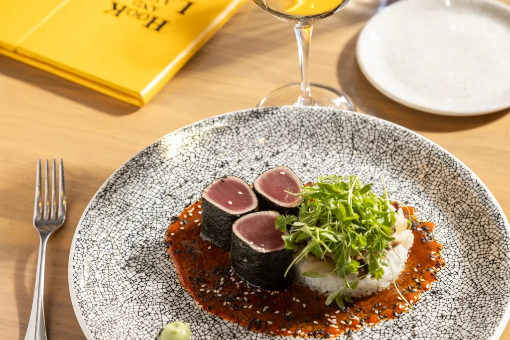 Rare seared tuna slices, rice, microgreens, and sauces on a patterned plate.