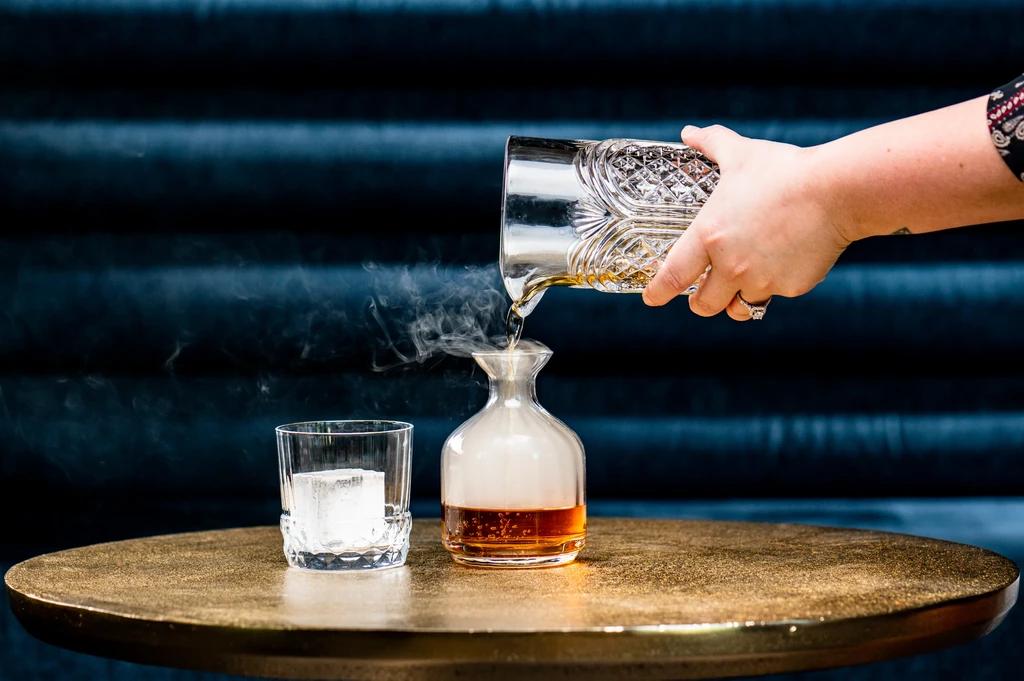 Close-up of a hand pouring a smoked whiskey cocktail.