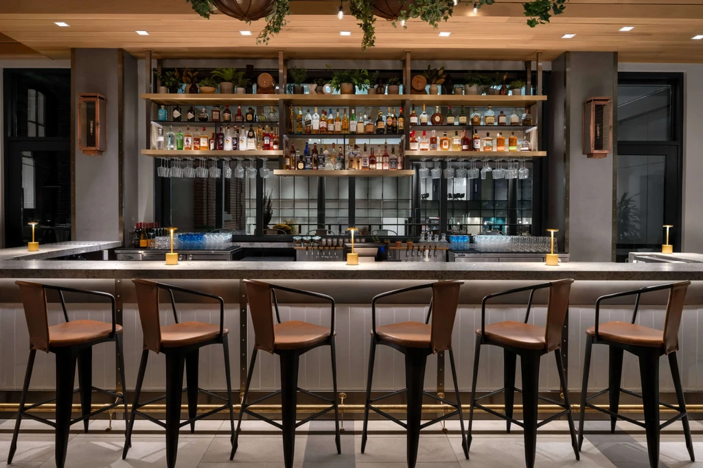 Modern bar with illuminated counter, seven stools, and liquor shelves.