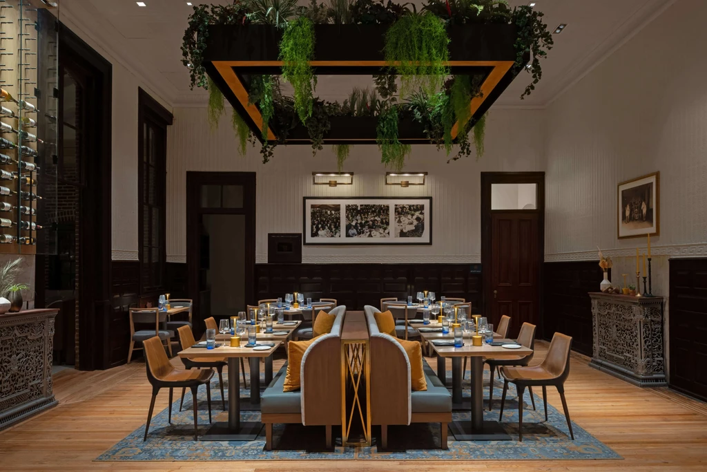 Elegant restaurant interior with tables set and lush overhead greenery.