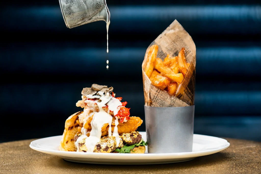 Elaborate lobster burger with truffle, gold leaf, and newspaper-wrapped fries.